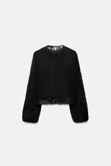 Blusa negra de cuello redondo y manga larga abullonada con elástico. Detalle de bordados con aplicación de abalorios. Cierre en espalda con aberturas y botones.