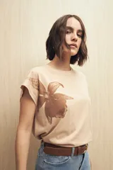 Remera blanca de manga corta con estampado de una flor color durazno en el frente.