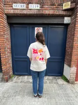 Remera color crema de corte oversize con estampado de flores y frutas en la espalda.