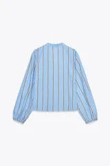 Camisa celeste con rayas verticales marrones y blancas, cuello redondo con escote en pico y mangas largas abullonadas. Cierre frontal con lazos con pespuntes marcados.