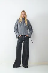 Jean wide leg de denim gris oscuro, con tiro medio, cierre de botón y cremallera. Presenta un diseño de pierna ancha con costuras decorativas en la parte delantera y ruedo deshilachado.