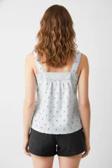 Blusa celeste con estampado de flores pequeñas, breteles anchos y escote cuadrado con detalle de puntilla. Cierre frontal con botones.