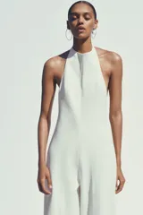 Mono largo blanco de cuello halter con botones y espalda descubierta. Pierna ancha y cierre trasero con cremallera oculta.