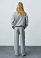 Pantalón gris de tiro medio y corte ancho, con bolsillos laterales, cierre oculto con botón, gancho y cremallera, y forro interior.