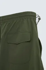 Pantalón verde militar de corte relaxed fit confeccionado en tejido técnico ligero. Cuenta con cintura elástica ajustable con cordón interior, bolsillos frontales y traseros con solapa, pliegues en las rodillas y bajo ajustable con elástico.