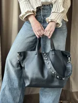 Cartera tipo tote bag color bordó, confeccionada en cuero con textura granulada. Tiene doble asa corta de mano y asa larga extraíble con diseño de tachas para usar como bandolera.