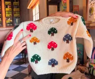 Sweater tejido de lana merino color crema con cuello redondo y diseño de hongos bordados a mano en colores azul, rojo, mostaza y verde.