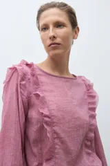 Blusa de manga larga color rosado con textura, escote redondo y volados decorativos en los hombros y a lo largo del frente.