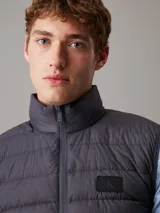 Chaleco negro de nailon ripstop con cuello alto, cierre de cremallera, bolsillos con cremallera en la cintura, aislante ligero de plumas y monograma de Calvin Klein estampado en el pecho.