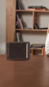 Billetera de cuero marrón oscuro con costuras artesanales en hilo blanco. Interior con compartimentos para billetes, visor y tarjeteros.