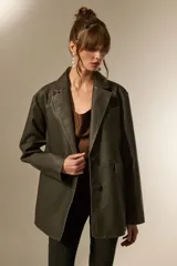 Blazer de eco-cuero color verde oliva oscuro, con efecto lavado, corte holgado, cuello solapa y dos botones frontales. Presenta pespuntes contrastantes y bolsillos de parche.