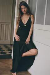 Vestido largo de satén negro, con escote en pico, tirantes finos dobles, abertura en la espalda y bajo asimétrico. Cierre lateral con cremallera oculta.