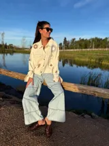 Campera de jean color manteca con apliques de flores de crochet en tonos neutros, corte recto y cierre con botones.