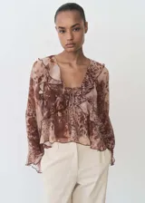 Blusa de gasa con estampado animal print en tonos marrones, cuello de pico con cierre de lazo, volantes en cuello y mangas largas acampanadas.