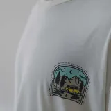Remera color crema con estampa en la espalda de una combi amarilla en un paisaje de montaña.