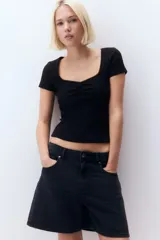 Remera corta negra de punto suave, corte ajustado, con costura fruncida en el centro del busto y escote corazón pronunciado con ribete de picot.
