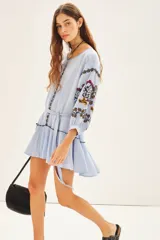 Vestido corto celeste de bambula con viso interno a tono, escote redondo con cartera y cinturón de tela base, detalle de volado en el ruedo y bordado en el frente y mangas.