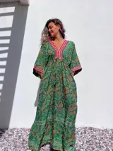 Vestido túnica largo con estampado paisley en tonos verdes, amarillos y rojos. Presenta escote en V con bordado decorativo y mangas 3/4 amplias.