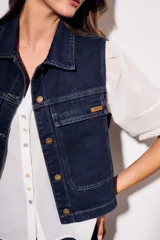 Chaleco de jean azul oscuro con cuello, bolsillos frontales y cierre con botones dorados. Corte al cuerpo.