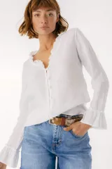 Blusa blanca de lino con botones de nácar, volados en el escote y mangas largas con puños acampanados. Corte recto y holgado.