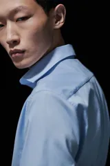 Camisa celeste de algodón con cuello italiano, tapeta clásica y canesú en la espalda. Mangas largas con tapeta y botón, y cierre ajustable de botón en los puños. Bajo levemente redondeado. Corte ajustado que realza el contorno del cuerpo creando una silueta entallada.