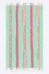 Toalla de playa de algodón, color verde menta, con rayas verticales en tonos rosados y marrones. Las rayas contienen texto repetido de la marca Bimba y Lola. Presenta flecos en los bordes cortos.