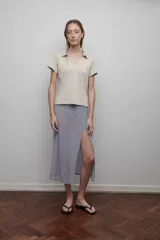 Camiseta confeccionada en remería de algodón, color beige, con cuello tipo polo y escote en V. Presenta dos líneas aplicadas en los laterales de cada manga.