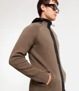 Cardigan de punto color marrón topo, con capucha negra contrastante y cierre frontal de cremallera negra. Presenta bolsillos laterales.