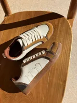 Championes urbanos de cuero color blanco hueso con detalles en marrón. Presentan cordones de algodón color crudo y logo bordado en el lateral.