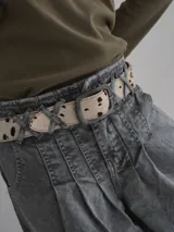 Cinturón de cuero sintético con estampado animal print de vaca en tonos marrones y blancos. Hebilla metálica plateada con logo grabado.