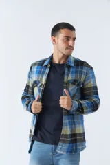 Sobrecamisa de algodón para hombre con interior de corderito, estampado a cuadros en tonos negro, blanco y azul. Tiene cierre de botones, bolsillos tipo cartera y logo en goma. El modelo usa talle M.