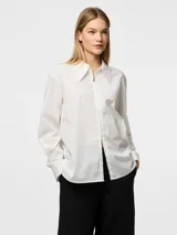Camisa blanca de corte holgado, con cuello clásico, mangas largas con puños abotonados y cierre frontal con cremallera.