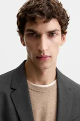 Blazer slim fit color gris oscuro confeccionado en tejido con viscosa. Tiene cuello con solapas de muesca, manga larga con puño abotonado, bolsillo de vivo en pecho, bolsillos de solapa en cadera, bolsillo interior, bajo con aberturas en espalda y cierre frontal con botones.