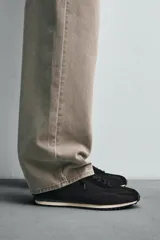Zapatilla de cordones negra de estilo retro. Parte superior fabricada en tejido técnico y detalles en piel con acabado serraje. Suela dentada con detalle a contraste.