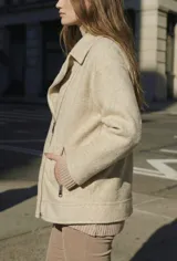 Campera de abrigo color crema, con cuello solapa y cierre frontal asimétrico. Presenta textura bouclé o de lana rizada.