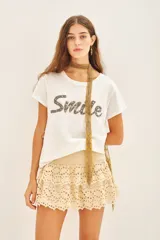 Remera blanca de algodón con bordado frontal de mostacillas metálicas formando la palabra "Smile".