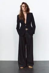 Blazer negra entallada con cuello solapa, manga larga con hombreras, bolsillos delanteros con solapa y cierre frontal con botones dorados.