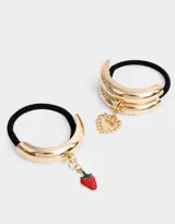 Set de dos gomitas de pelo elásticas negras con apliques metálicos dorados y dijes colgantes: una con dije de corazón y otra con dije de pimiento rojo.
