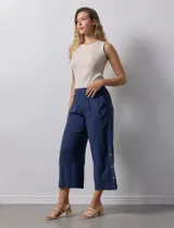Pantalón blanco de algodón con pretina elastizada, bolsillos inclinados y ruedo lateral con tajo y botones.