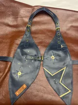 Top de cuero azul con diseño de estrellas doradas y la letra S en el frente. Se ajusta en hombros, busto y espalda.