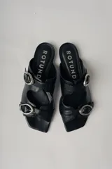 Sandalias planas de cuero color marrón con dos tiras anchas sobre el empeine, cada una con hebilla dorada.