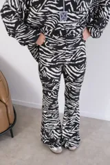 Conjunto de pantalón y camisa con estampado animal print tipo cebra en blanco y negro. La camisa es de manga larga con cierre de cremallera y el pantalón es acampanado.