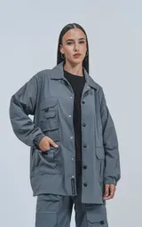 Campera gris con broches en el delantero, forrada con red, múltiples bolsillos con detalles en réflex y puños elásticos en las mangas. Confeccionada en textil liviano 100% poliéster y calce oversize.