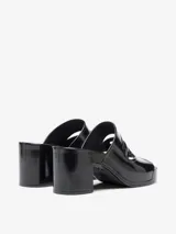 Sandalia tipo mule negra de charol, con plataforma y taco ancho. Presenta un diseño calado en la parte superior con un corte que simula un logo o forma geométrica.