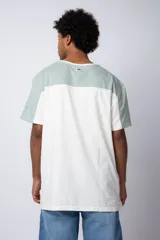 Remera color beige con mangas y parte superior en verde militar. Estampado frontal con texto "Lucky" y diseño de flores con rostro.