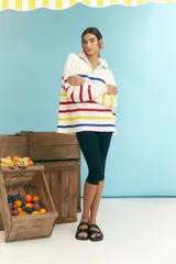 Sweater de punto grueso color crudo, con cuello alto con cierre de cremallera y rayas horizontales en azul, amarillo y rojo.