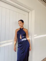 Vestido largo azul con escote halter cruzado, abertura en el pecho, falda drapeada con flecos y corte irregular.