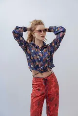 Camisa crop azul con estampado floral multicolor, cuello camisero, mangas largas con puños abotonados y lazos para atar en la cintura.