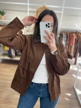 Chaqueta marrón de símil gamuza con cuello de cuerina, cierre frontal, bolsillos con solapa y elástico ajustable en la cintura.