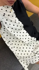 Vestido corto sin mangas, con escote recto y corte a la rodilla. Presenta un diseño bicolor, con un lado blanco con lunares negros y otro lado negro liso.